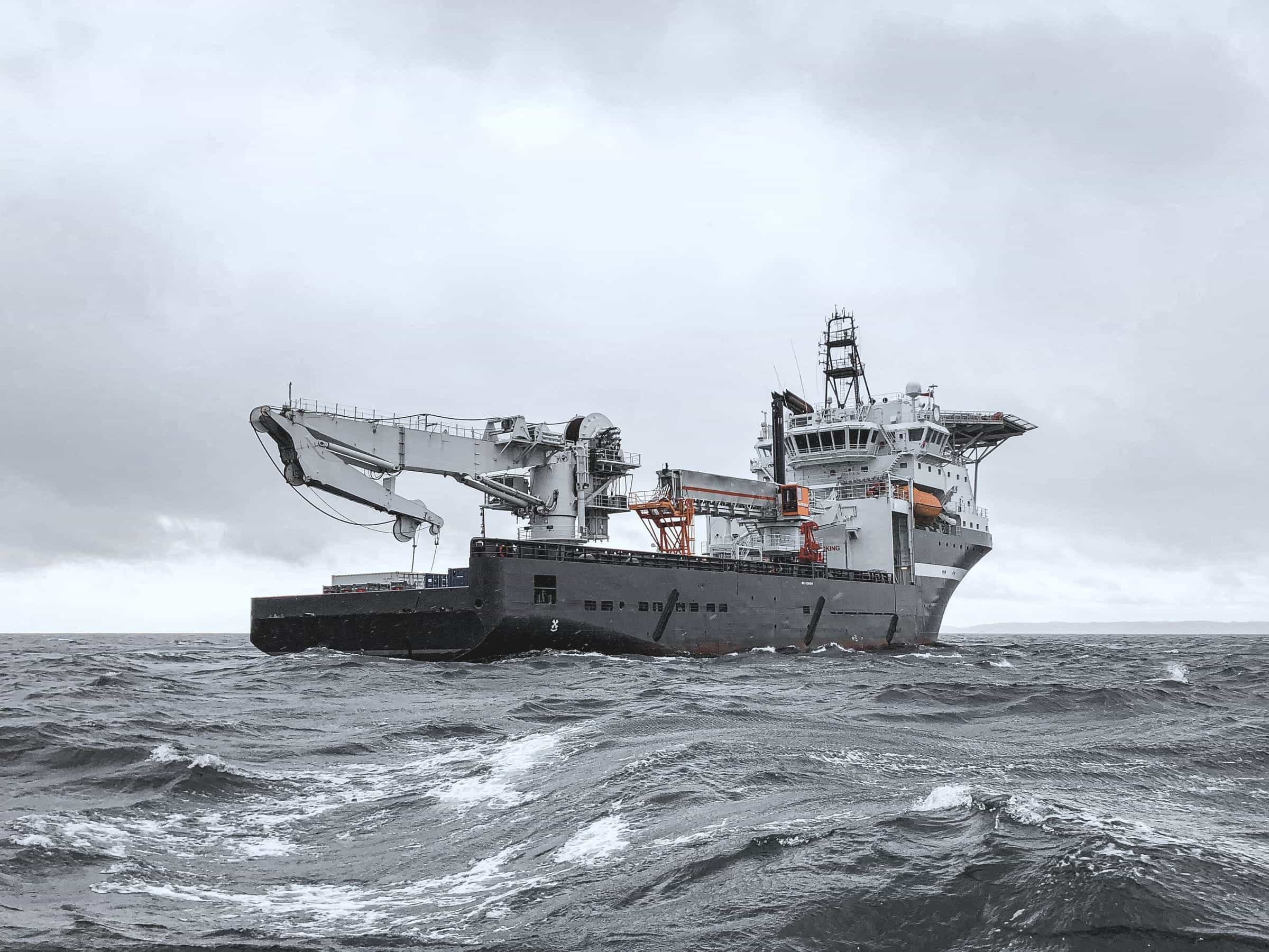 Konstruksjonsfartøy med offshorekran i grå sjø under overskyet himmel